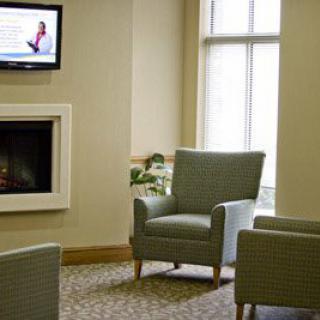 A cozy waiting room with comfortable chairs, a wall-mounted television, and natural lighting from large windows.