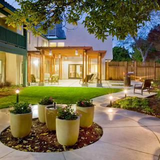 A beautifully landscaped backyard with a patio and garden, illuminated by evening lights.