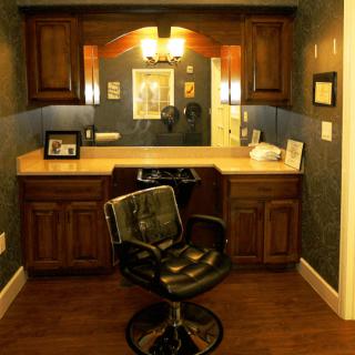 A cozy barbershop setup with a classic barber chair facing a well-lit vanity mirror and surrounded by wooden cabinets.