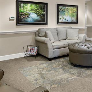 A cozy living room with a sofa, large ottoman, and nature-themed paintings on the wall.