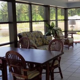 A cozy sunroom with large windows, featuring a table with chairs and a comfortable sofa.