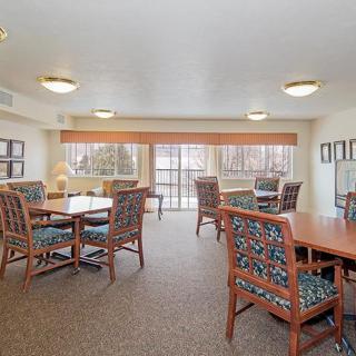 A well-lit communal living room with several tables and chairs, featuring large windows for natural light.