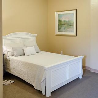 A minimalist bedroom with a white bed and a framed picture on the wall.