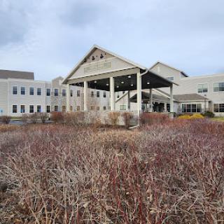A modern building with a distinctive architectural design surrounded by barren shrubs under a cloudy sky.