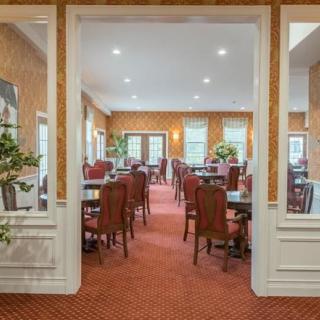 A cozy dining room with wooden tables and chairs, complemented by a carpeted floor and decorative plants.