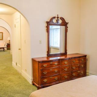 A traditional bedroom interior featuring a wooden dresser with an attached mirror on green carpeted flooring.