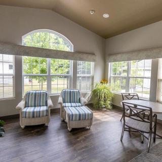 A bright and airy living room featuring two striped chairs, large windows, and a small dining area.