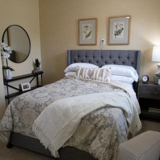 A cozy bedroom with a neatly made bed, decorative pillows, artwork on the walls, and a side table with a lamp.