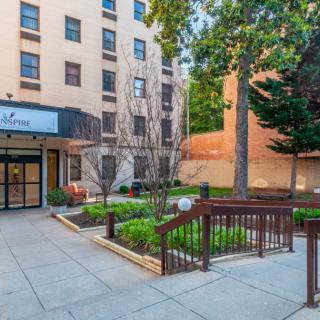 Entrance of an apartment building with landscaped surroundings and sidewalk.