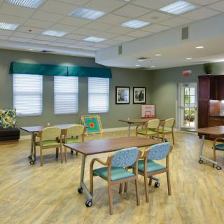 A spacious dining room with tables and chairs, featuring large windows and bright lighting.