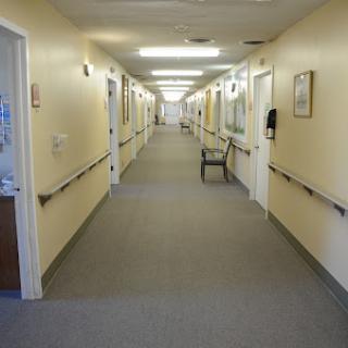 A long, empty hallway in a healthcare facility, featuring walls with light colors and overhead lighting.