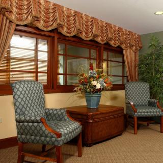 A cozy living room with two patterned chairs, a wooden table, and floral decorations by the window.