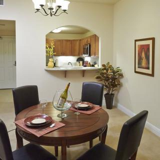 A cozy dining room with a round table set for two, featuring a view into the kitchen.