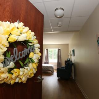 A welcoming wreath hangs on an open door leading to a cozy bedroom.