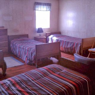 A cozy bedroom featuring three beds with striped bedding and natural light coming in through the window.