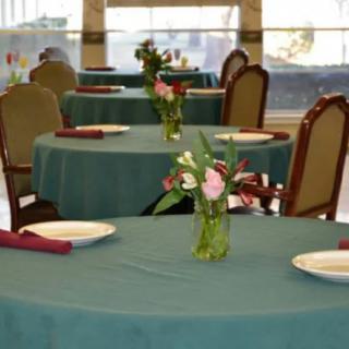 A neatly arranged dining area with tables set for guests, featuring vases of flowers as centerpieces.