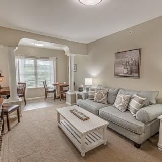 A cozy living room with a sofa, coffee table, and adjoining dining area, featuring neutral tones and soft lighting.