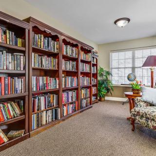 A cozy library room with tall bookshelves filled with books, a comfortable reading chair, and a large window letting in natural light.