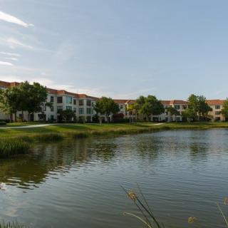 A serene view of an apartment complex by a lake, surrounded by lush greenery.
