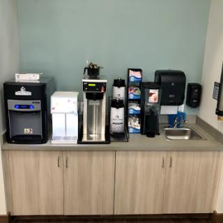 A well-equipped beverage station in an office break room featuring various coffee and water machines.