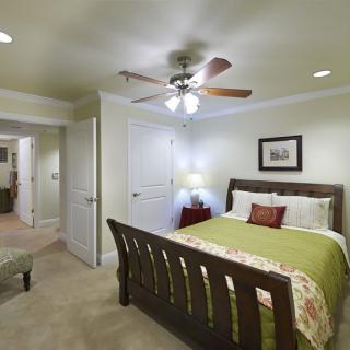 A cozy bedroom featuring a wooden bed with green bedding, a ceiling fan, and soft lighting.