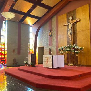 A church interior featuring an altar with a crucifix and stained glass windows.