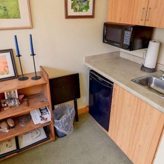 A compact kitchenette with a microwave, mini fridge, and wooden cabinets, alongside a bookshelf topped with candlesticks.