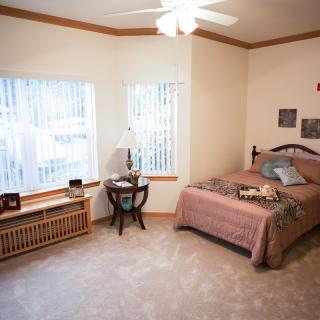 A cozy bedroom with a single bed, large windows, and simple decor.