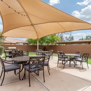 A sunny outdoor patio with tables and chairs under a large shade sail.
