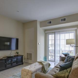 A cozy living room with a sofa facing a wall-mounted TV and a sliding glass door leading outside.