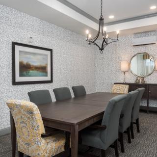 A modern dining room with a long wooden table, upholstered chairs, a stylish chandelier, and decorative wall art and mirror.