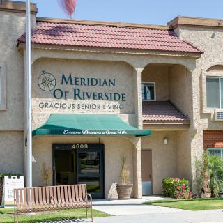 Entrance of the Meridian of Riverside senior living facility with an awning and landscaped surroundings.