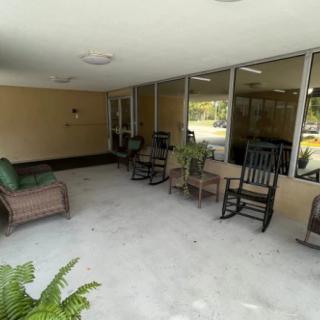 A covered porch with rocking chairs and wicker furniture, featuring several potted plants.