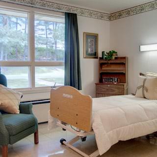 A cozy hospital room with a single bed, armchair, and large window providing natural light.