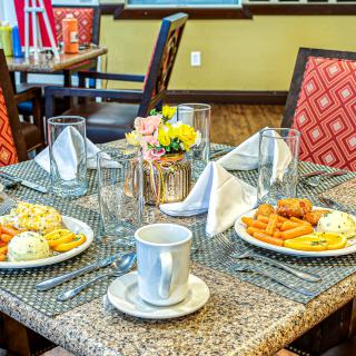 A dining table set for breakfast with plates, cups, and decorative flowers.