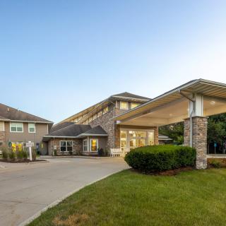 A modern building with a covered entrance and driveway, surrounded by greenery.