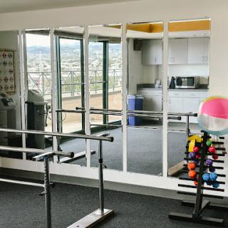 A well-equipped gym featuring a barre, colorful weights, and large mirrors reflecting the workout area.