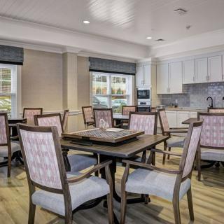 A well-lit dining area featuring multiple tables and chairs, adjacent to a kitchenette.