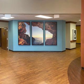 A welcoming hospital lobby featuring large landscape artwork and a warm wooden floor.