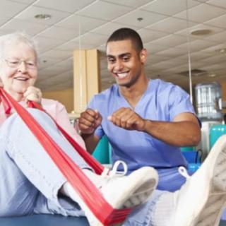 A healthcare professional assists an elderly woman with physical therapy exercises using a resistance band.