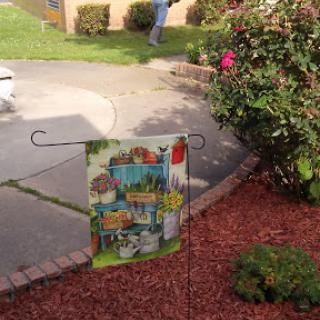 A colorful garden flag displayed in a lush outdoor setting.