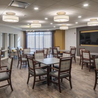 A modern dining room with neatly arranged tables and chairs, illuminated by ceiling lights.
