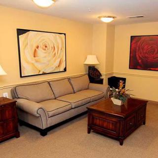 A cozy living room with a sofa, wooden tables, decorative lamps, and floral artwork on the walls.