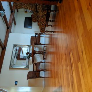 A dining room with a wooden floor, table, and chairs, featuring a large mirror on the wall.