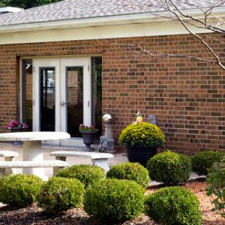 A charming outdoor patio area with well-manicured bushes and a brick building in the background.
