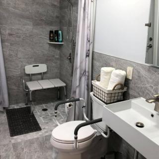 A modern, accessible bathroom featuring a shower chair and grab bars.