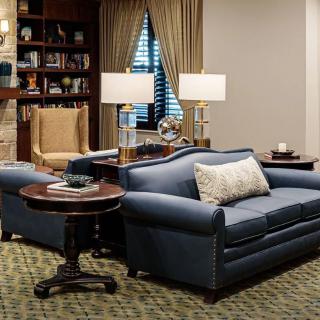 A cozy living room with a blue sofa, lamps, and a bookshelf.