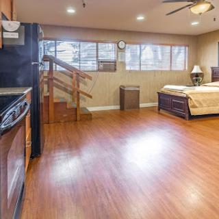 A spacious studio apartment featuring a kitchenette, wooden flooring, and ample natural light.