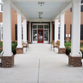 A covered walkway with benches leading to a red door entrance.
