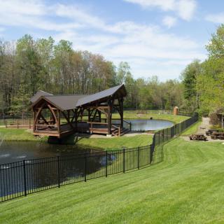 A scenic view of a wooden bridge over a pond surrounded by lush greenery and a black metal fence.